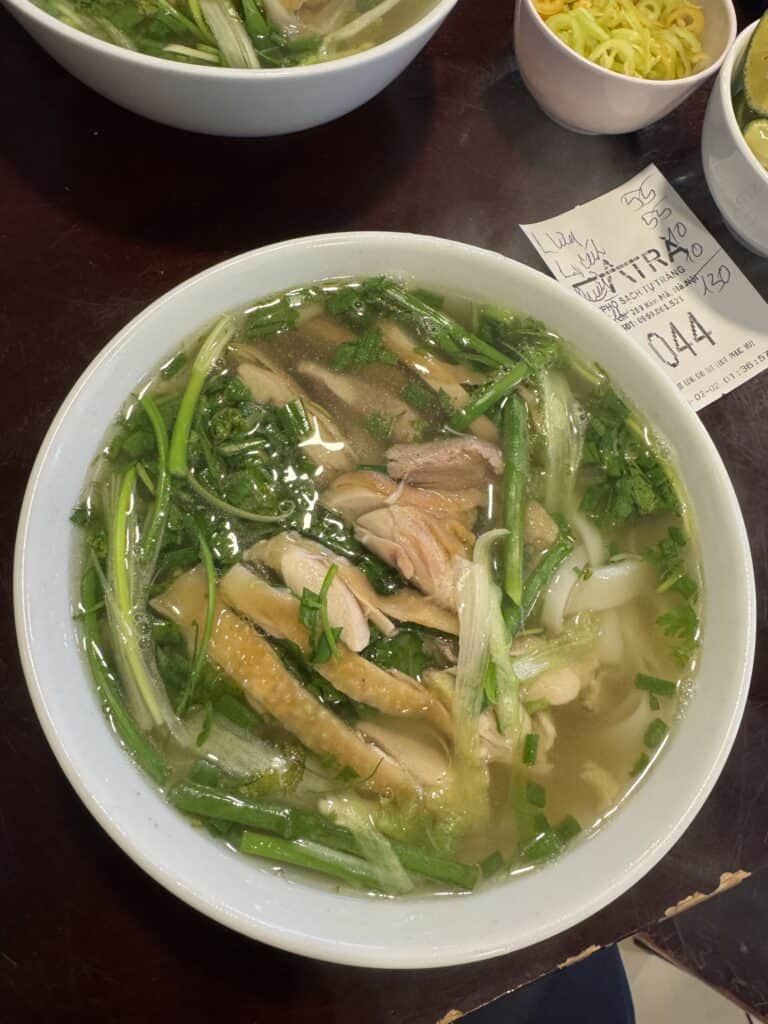 Vietnamese chicken noodle soup with fresh herbs and green vegetables, served hot in a white bowl.